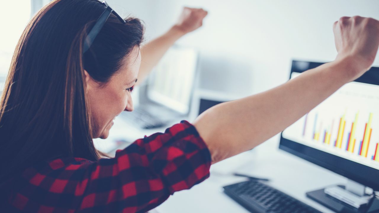 Woman looking at computer screen with arms raised and a smile