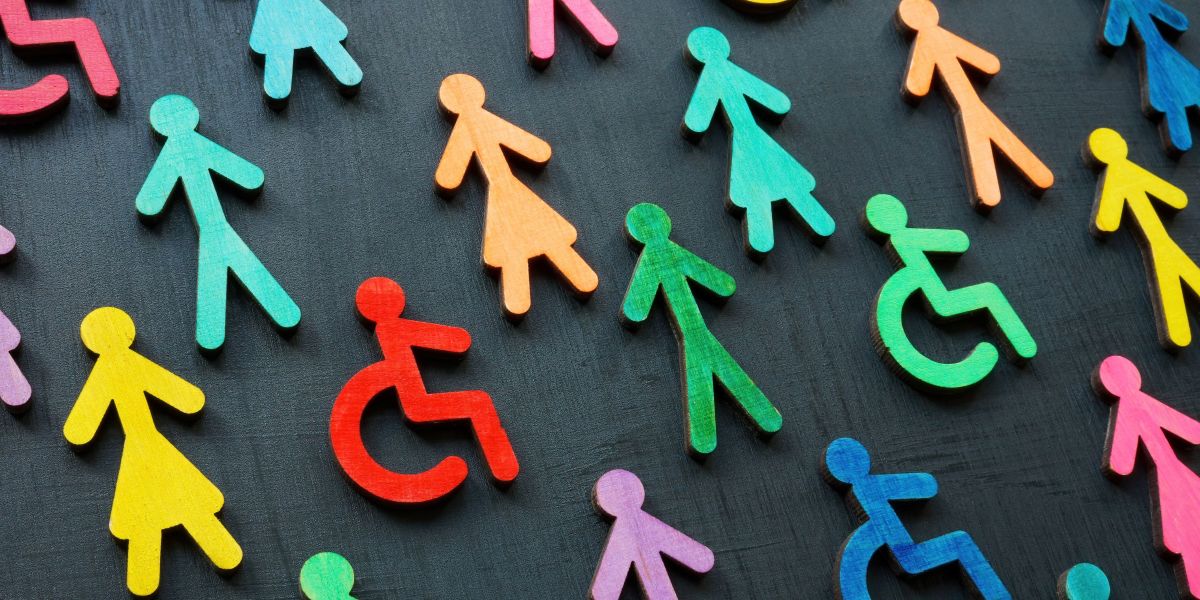 Colourful wooden figures, including wheelchair-user symbols, arranged on a dark background.